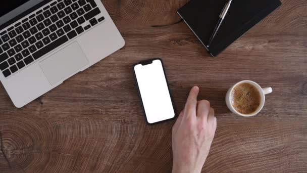 白い画面のスマートフォンを使用した男性の手のトップビュー 上からのフリーランスのワークスペース 選択的フォーカス — ストック動画