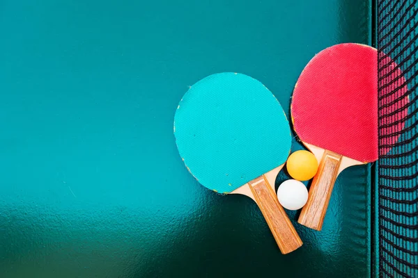 緑のテーブルの表面にテーブルテニスラケットとピンポンボールネット 選択的フォーカス — ストック写真