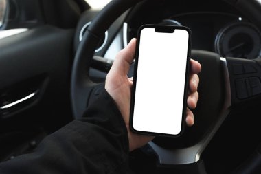 Arabada akıllı telefon kullanan erkek sürücü, kopyalama alanı olarak boş beyaz ekranlı mobil cihaz, seçici odak