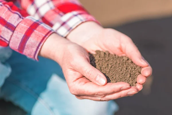 Handful of fertile soil, farm worker holding plowed dirt in hands and checking the quality before seeding season