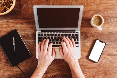 Freelancer working on laptop computer in home office, top view flat lay with smartphone mockup screen