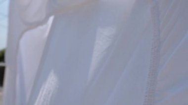 Beyaz kötü çarşaf rüzgarda ve ılık yaz güneşinde kurumak için asılı, seçici odaklı ağır çekim