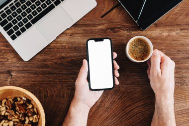 Freelancer boş beyaz ekran ile cep telefonu kullanıyor ve ofis masasında kahve içiyor.