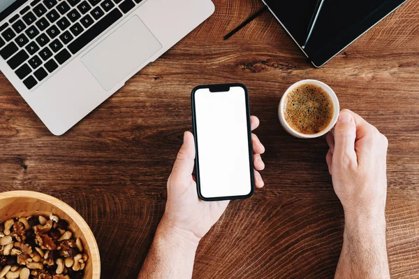 Freelancer boş beyaz ekran ile cep telefonu kullanıyor ve ofis masasında kahve içiyor.