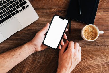 Freelancer ofis masasında boş beyaz maket ekranlı cep telefonu kullanıyor.