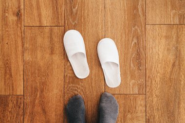 Erkek ayakları ve tek kullanımlık beyaz terlikler otel odasında.