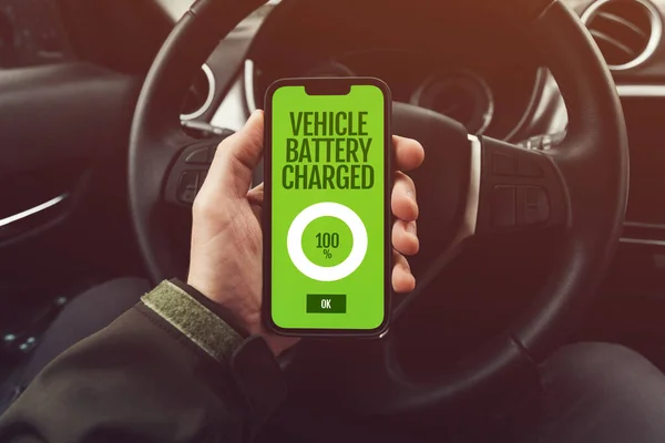 Vehicle battery charged at full 100% message on smartphone app screen held by electric car driver, selective focus