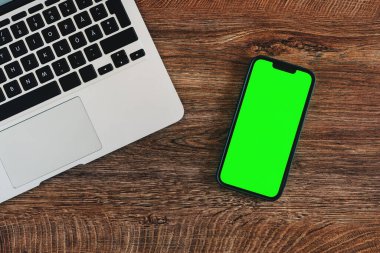 Ofis masasında boş yeşil dokunmatik ekran ve dizüstü bilgisayarı olan cep telefonu, iş iletişimi ve bağlantı konsepti için kopyalama alanı olan üst görünüm düzlüğü