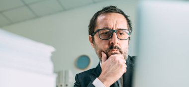 İş yerinde dizüstü bilgisayara bakan endişeli iş adamının panoramik portresi, seçici odaklanma