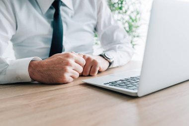 Ofis masasında dizüstü bilgisayarın önünde yumruklarını sıkan bir iş adamı.