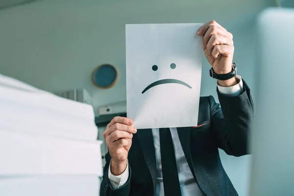 Unhappy Businessman Holding Paper Frowning Emoticon Office Interior Selective Focus —  Fotos de Stock