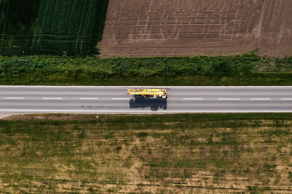 Crane truck or boom-truck on the road through countryside landscape, aerial shot from drone pov, directly above