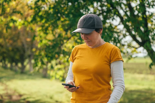 Ceviz Ağacının Meyve Bahçesinde Akıllı Telefon Kullanan Turuncu Tişört Giyen — Stok fotoğraf