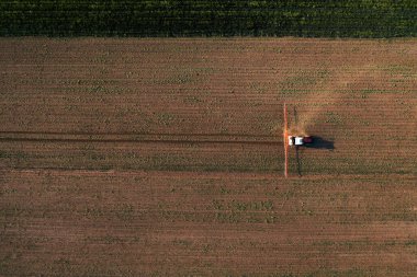Tarımsal traktörün ekin püskürtücüsüyle havadan çekilmiş görüntüsü mısır tarlasının üzerine bitki öldürücü kimyasallar sıkıyor.