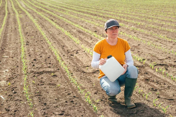 Corn crop protection concept, female farmer agronomist holding jerry can container canister with pesticide, selective focus