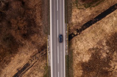 Aerial view of black car on the highway bridge over small creek, top view drone pov