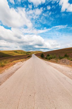 Empty asphalt road through beautiful Zlatibor region landscape stretching in diminishing perspective and disappearing behind the green hill of this famous Serbian tourist resort on sunny summer day