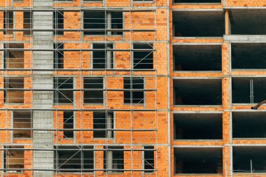 Construction industry and apartment building development, scaffolding surrounding tall built structure made of concrete and clay blocks in residential area