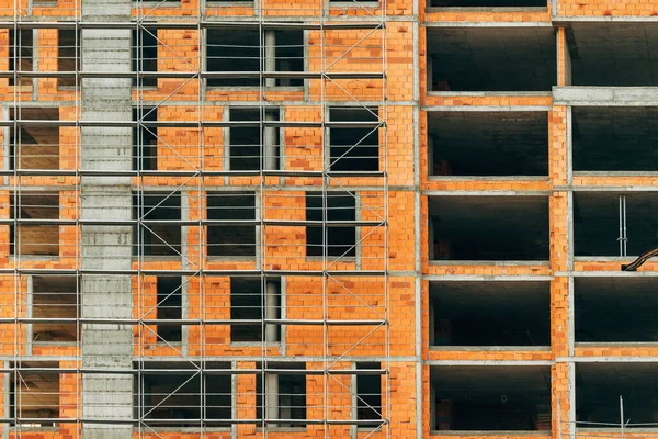 Construction industry and apartment building development, scaffolding surrounding tall built structure made of concrete and clay blocks in residential area