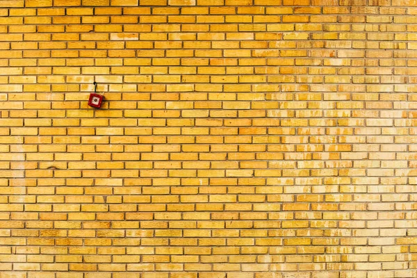 Yellow brick wall with fire alarm button as background