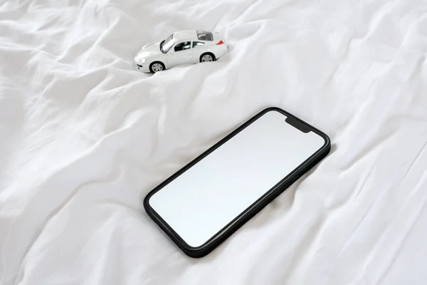 スマートフォンとベッドの上でモデル車を死ぬ コピースペースとして空白の白いモックアップ画面を持つ携帯電話デバイス 選択的焦点 — ストック写真