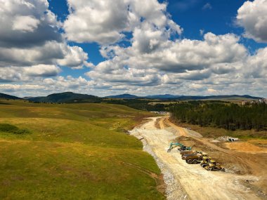 Zlatibor 'da yol yapımı ve ağır endüstriyel makineler güneşli yaz gününde İHA pov' un hava görüntüsü.