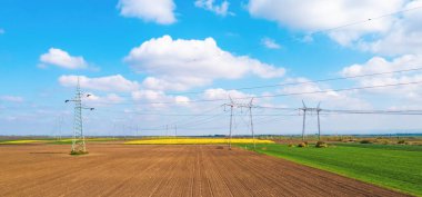 Aerial shot of transmission towers electricity pylons with power lines in cultivated agricultural field, drone pov high angle view