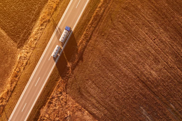 Aerial shot of cistern truck for milk transportation driving along the non-urban landscape in autumn afternoon, drone pov directly above