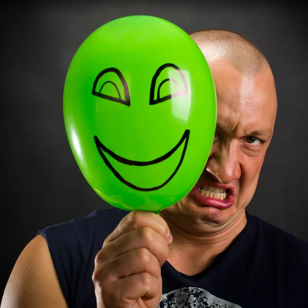 Θυμωμένος άνθρωπος που κρύβονται πίσω από την ευτυχισμένη μπαλόνι — Φωτογραφία Αρχείου