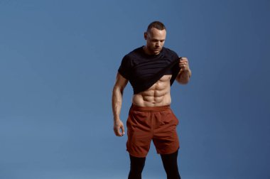 Kaslı erkek sporcu stüdyoda karın kaslarını gösteriyor.