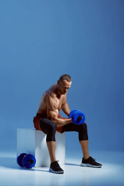 Atleta con mancuernas sentado en cubo en el estudio —  Fotos de Stock