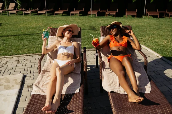 Girlfriends drink coctails on sun beds at pool — Stock Photo, Image