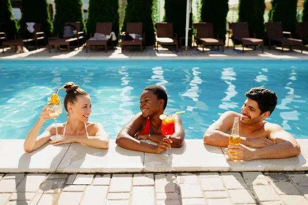 Amigos con bebidas posan al borde de la piscina — Foto de Stock