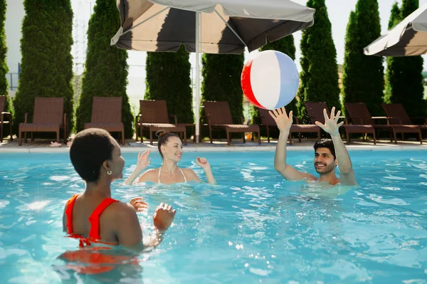 Amici sorridenti giocano con la palla in piscina — Foto Stock