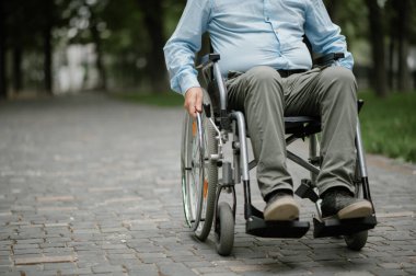 Tekerlekli sandalyedeki engelli adam parkta dinleniyor.