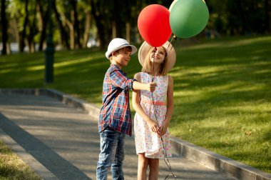 Kız ve erkek parkta hava balonlarıyla yürüyorlar.