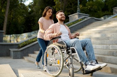 Tekerlekli sandalyeli çift parktaki merdivenlerden yukarı çıkıyor.