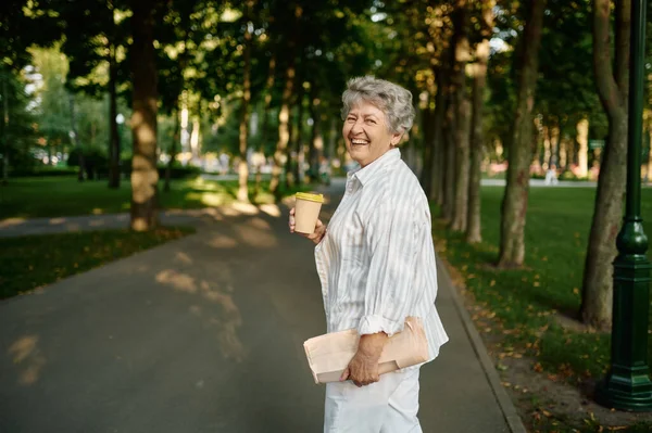 Funny granny drinks coffee in summer park