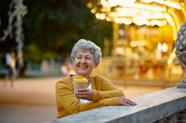 Бабуся п'є каву в літньому парку розваг — стокове фото