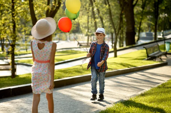 Boy and girl walking with air balloons in park — Stock Photo, Image