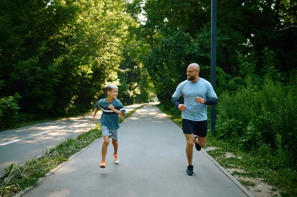 Ojciec i syn biegną ścieżką spacerową w parku — Zdjęcie stockowe