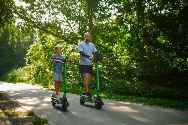 Vader en jongen rijden op kick scooters in het park — Stockfoto