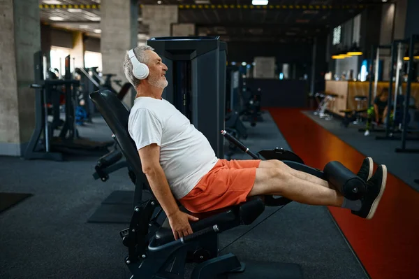 Homem idoso em fones de ouvido fazendo exercícios abdominais — Fotografia de Stock