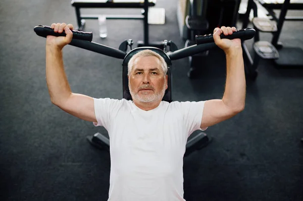 Elderly man, workout on exercise machine, gym