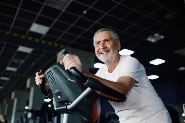 Starszy mężczyzna pozuje na rowerze treningowym w siłowni — Zdjęcie stockowe