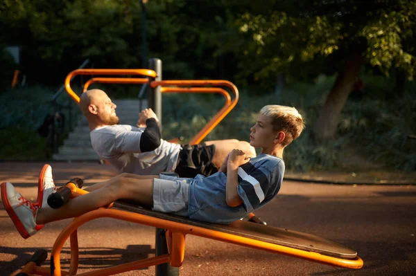 Отец и мальчик делают упражнения на прессе на детской площадке — стоковое фото