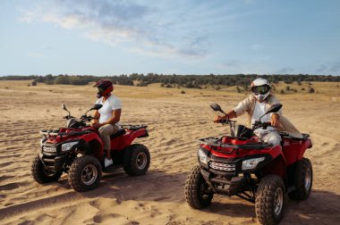 Kask takan iki adam çölde ATV 'ye biniyor.