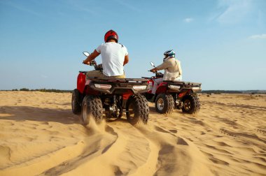 Çöl kumlarında ATV 'ye binen kasklı iki adam.