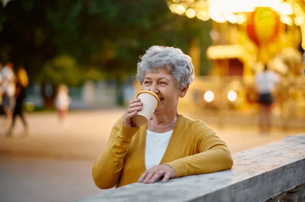 Бабуся п'є каву в літньому парку розваг — стокове фото