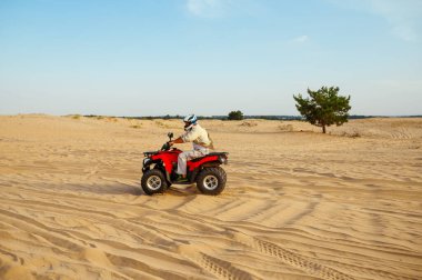 Kasklı bir adam çölde ATV 'ye biniyor.